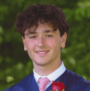 Young man in a blue graduation gown with a red rose, smiling outdoors.